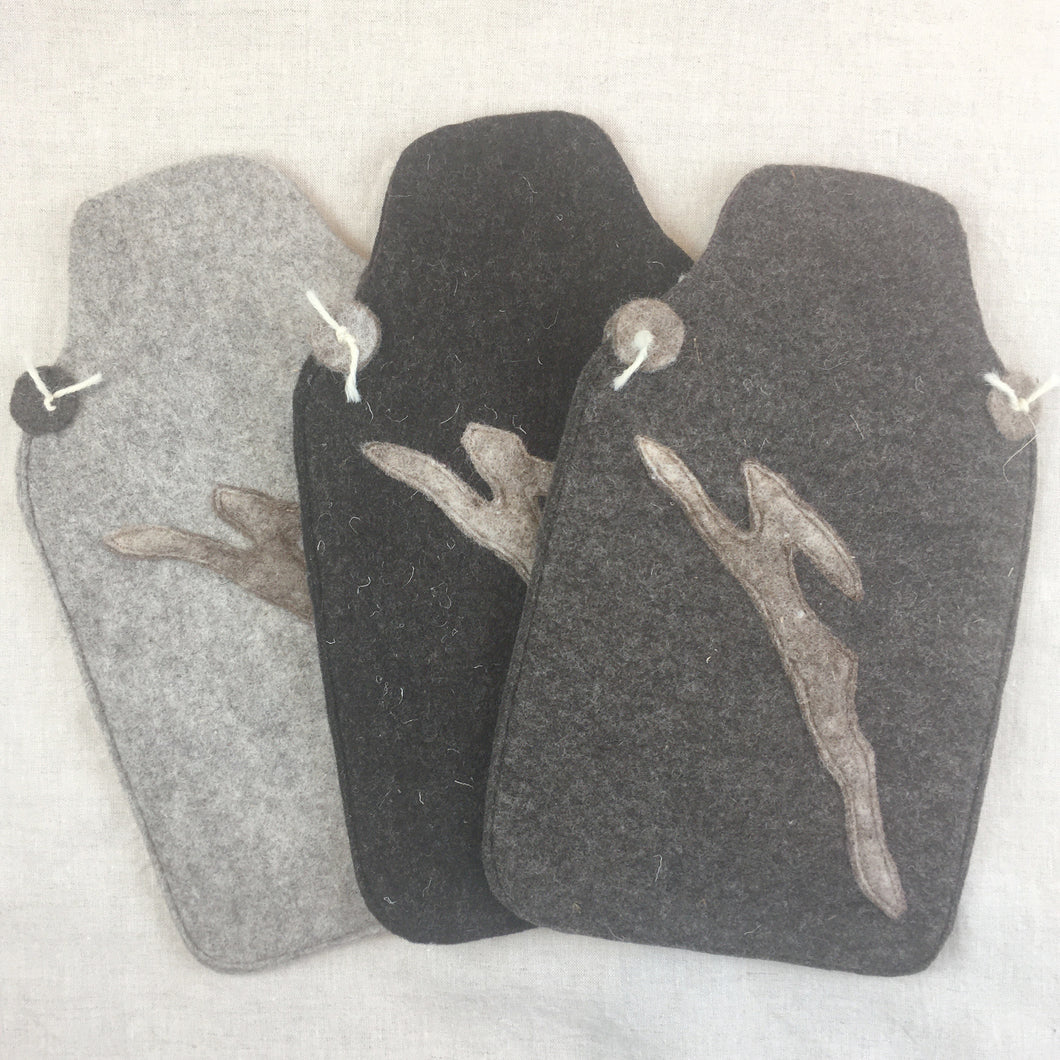 Three hot water bottle covers lying next to each other in different shades of grey and brown with a hare motif