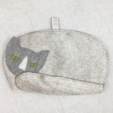 Load image into Gallery viewer, A photo of the cat shaped tea cosy laid flat against a smooth linen cloth. The cat has a pale grey body and dark grey head with green eyes. 

